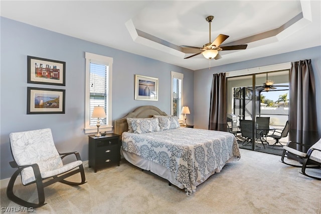 carpeted bedroom with access to exterior, ceiling fan, and a tray ceiling