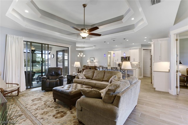 living room with ceiling fan with notable chandelier and a raised ceiling