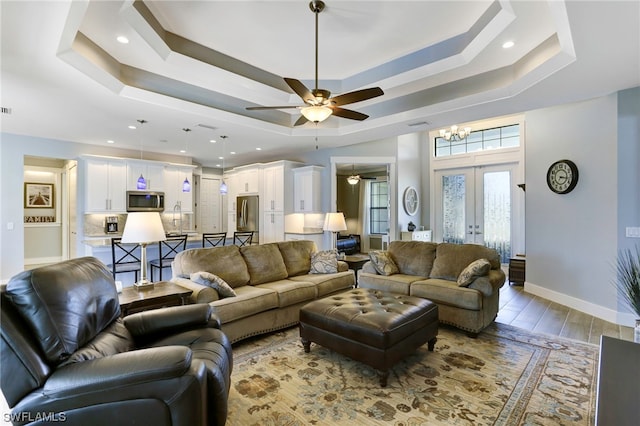 living room with ceiling fan with notable chandelier, a tray ceiling, french doors, and light hardwood / wood-style flooring