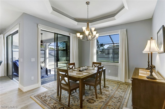 dining room with a tray ceiling, light wood-type flooring, and ceiling fan with notable chandelier