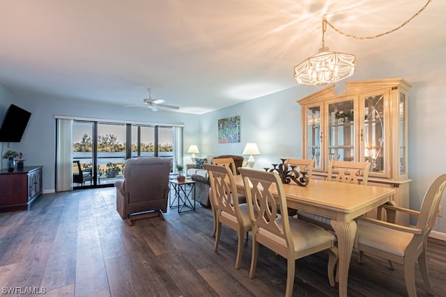 dining room featuring ceiling fan with notable chandelier, a water view, and dark wood-type flooring