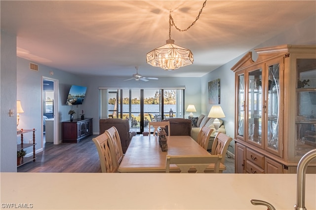 dining area with a water view, ceiling fan with notable chandelier, and dark wood-type flooring