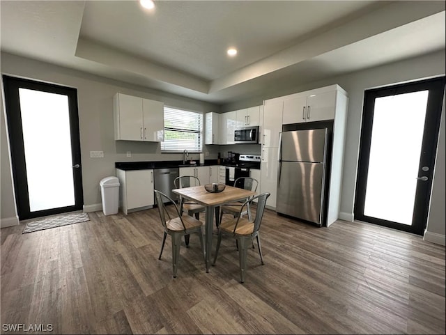 kitchen with a raised ceiling, appliances with stainless steel finishes, hardwood / wood-style floors, and white cabinetry