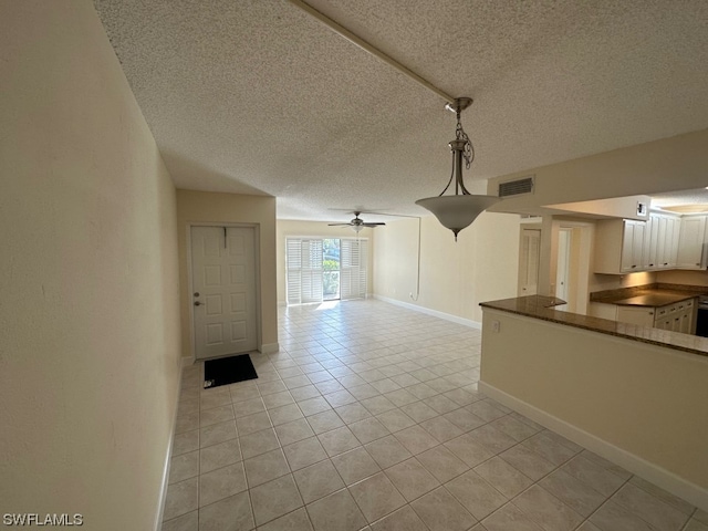 unfurnished living room with light tile floors, ceiling fan, and a textured ceiling