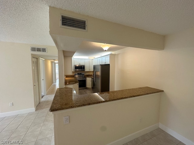 kitchen with stainless steel appliances, light tile floors, dark stone counters, kitchen peninsula, and white cabinetry