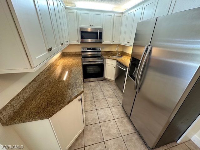 kitchen featuring dark stone countertops, white cabinets, light tile floors, and stainless steel appliances