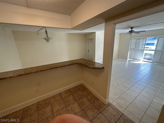 basement featuring light tile flooring, ceiling fan, and a textured ceiling