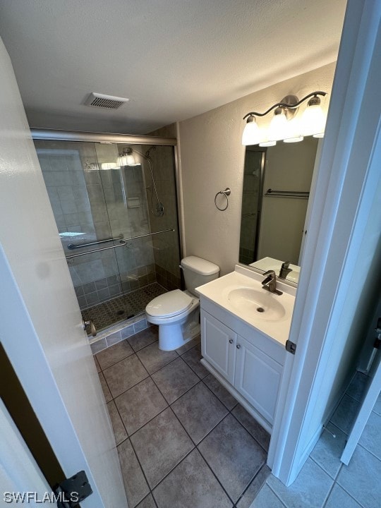 bathroom featuring toilet, a shower with door, tile flooring, and vanity