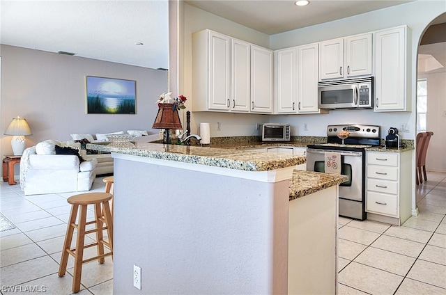 kitchen with light tile flooring, stainless steel appliances, kitchen peninsula, and a kitchen breakfast bar