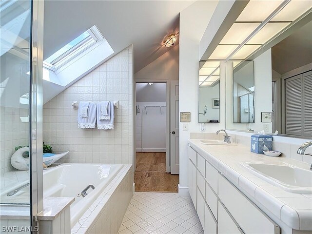 bathroom featuring dual bowl vanity, tile walls, a tub, vaulted ceiling with skylight, and hardwood / wood-style flooring