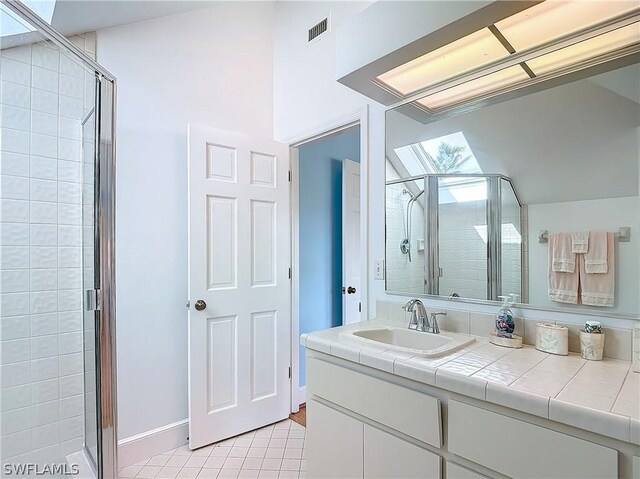 bathroom featuring a skylight, vanity, a shower with door, and tile patterned flooring