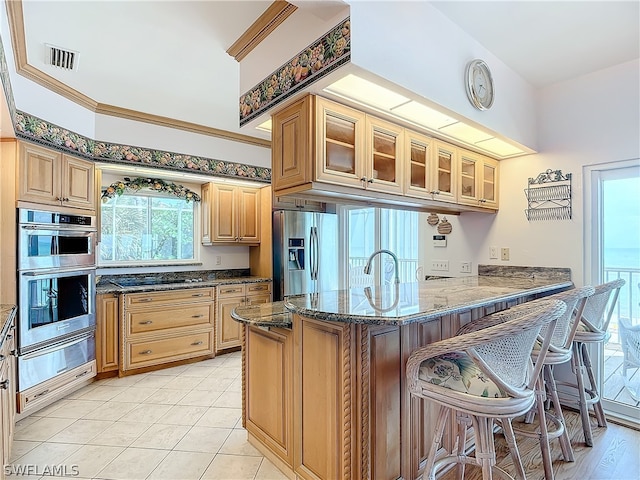 kitchen with a breakfast bar area, crown molding, kitchen peninsula, dark stone counters, and appliances with stainless steel finishes