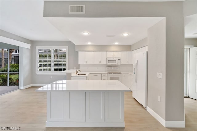 kitchen with white appliances, sink, light wood-type flooring, a kitchen island, and white cabinetry