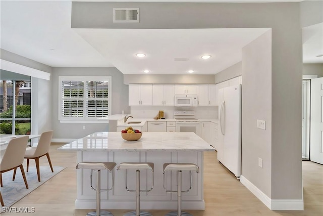 kitchen featuring white cabinetry, sink, light hardwood / wood-style floors, white appliances, and a breakfast bar area