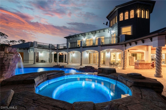 pool at dusk featuring an in ground hot tub, pool water feature, and a patio