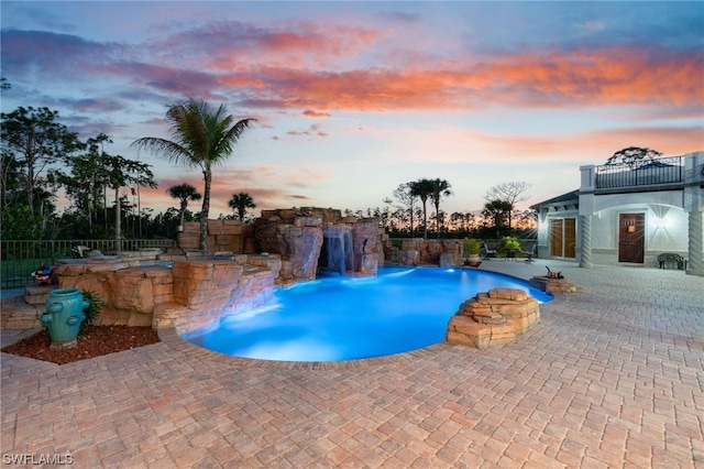 pool at dusk featuring pool water feature and a patio