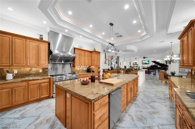 kitchen with a center island with sink, backsplash, a tray ceiling, and wall chimney range hood