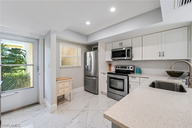 kitchen featuring backsplash, white cabinets, sink, light stone countertops, and appliances with stainless steel finishes