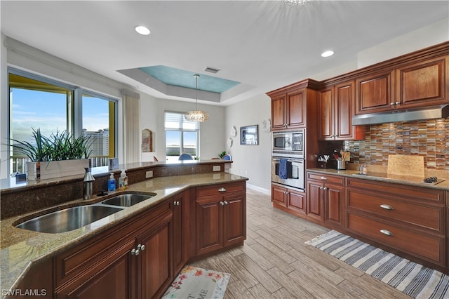 kitchen featuring light wood-type flooring, stainless steel appliances, sink, stone countertops, and a chandelier