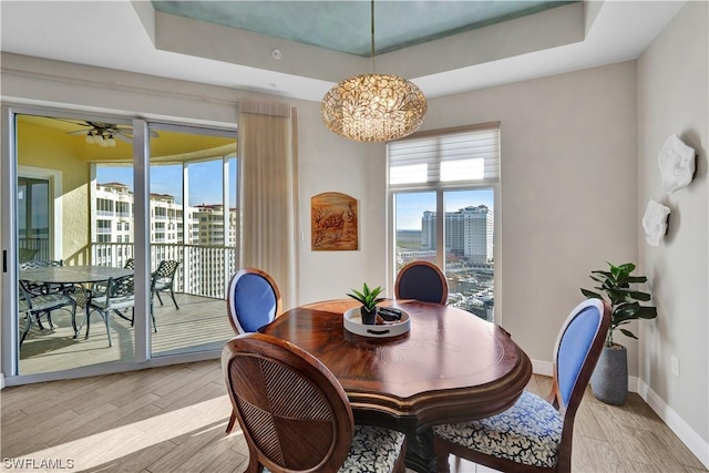 dining area with ceiling fan with notable chandelier, light wood-type flooring, and a tray ceiling