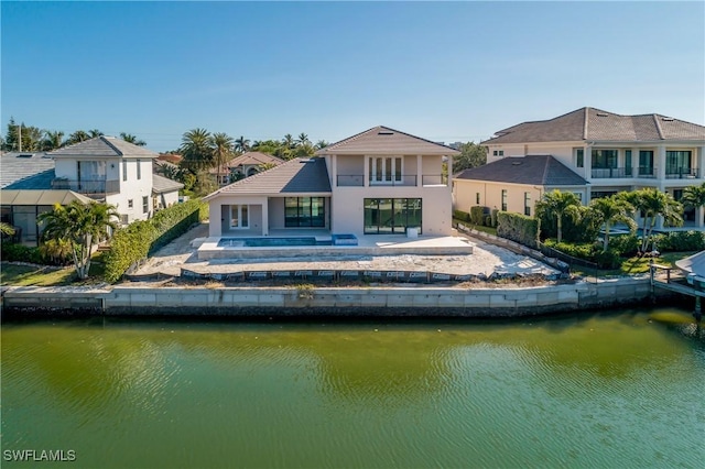 back of house with a jacuzzi, a balcony, and a water view