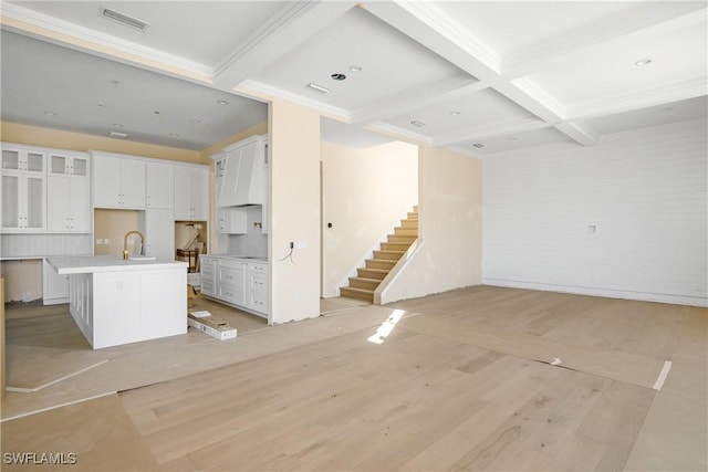 kitchen featuring a kitchen island with sink, coffered ceiling, sink, beamed ceiling, and white cabinetry