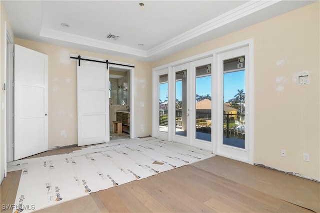 interior space with a barn door, a raised ceiling, and light hardwood / wood-style flooring