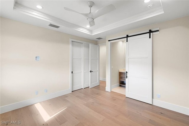 unfurnished bedroom with light wood finished floors, a barn door, a raised ceiling, and baseboards