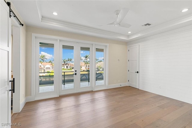 empty room featuring recessed lighting, a raised ceiling, a barn door, light wood-style floors, and a ceiling fan