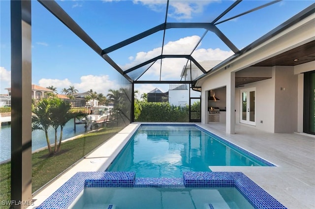 view of pool with a lanai, a water view, a pool with connected hot tub, exterior kitchen, and a patio area