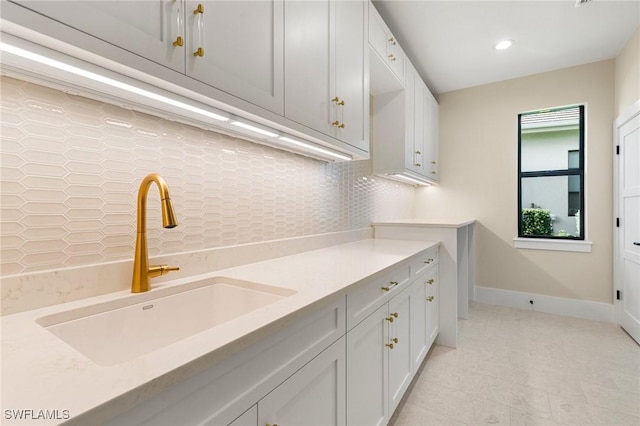 kitchen with baseboards, light countertops, a sink, and decorative backsplash