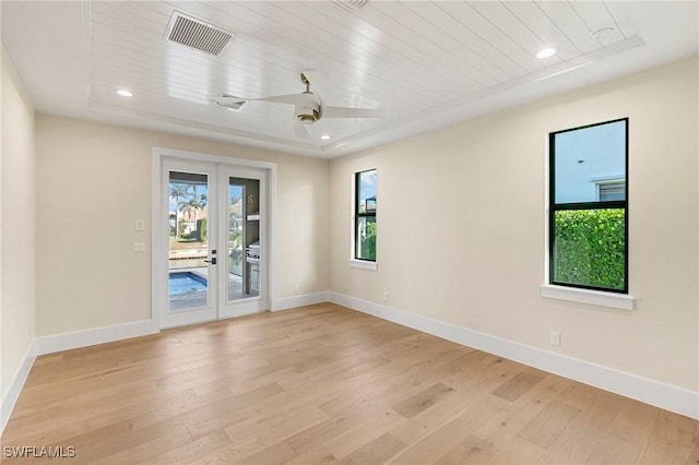 spare room featuring baseboards, light wood-style flooring, visible vents, and a tray ceiling