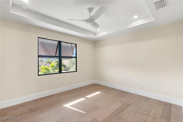 unfurnished room featuring a tray ceiling, visible vents, light wood-style floors, a ceiling fan, and baseboards