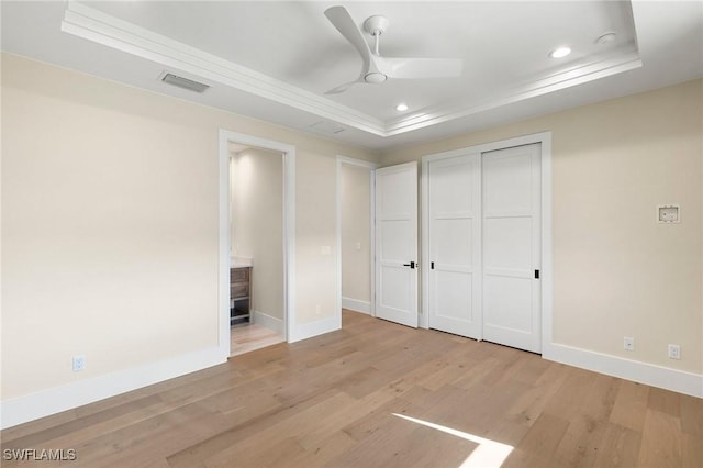 unfurnished bedroom featuring recessed lighting, light wood-type flooring, a raised ceiling, and baseboards