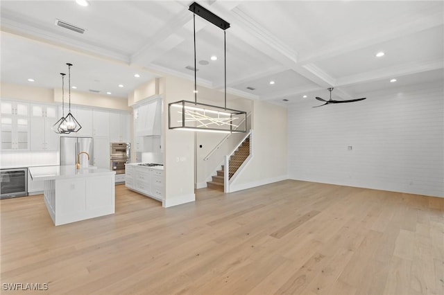 unfurnished living room with beam ceiling, light wood-style flooring, beverage cooler, coffered ceiling, and stairs