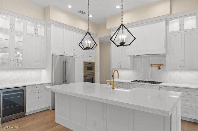 kitchen with an island with sink, wine cooler, glass insert cabinets, appliances with stainless steel finishes, and white cabinetry