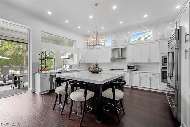 kitchen with pendant lighting, wall chimney range hood, stainless steel appliances, a notable chandelier, and dark hardwood / wood-style floors