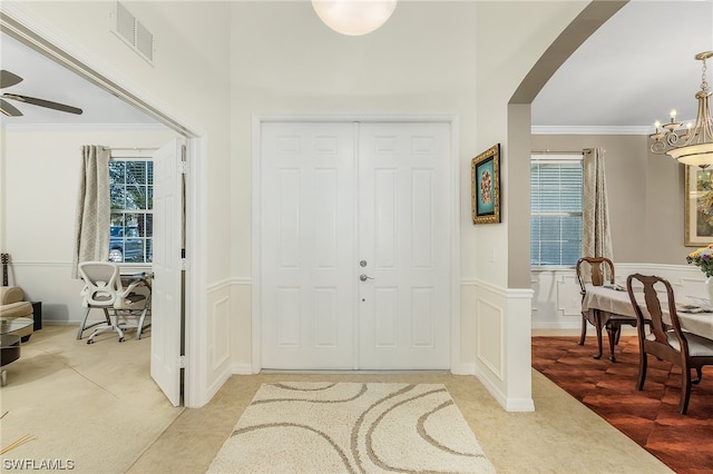 tiled foyer with crown molding and ceiling fan with notable chandelier