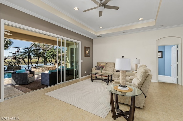 living room with light tile floors, a tray ceiling, ornamental molding, and ceiling fan