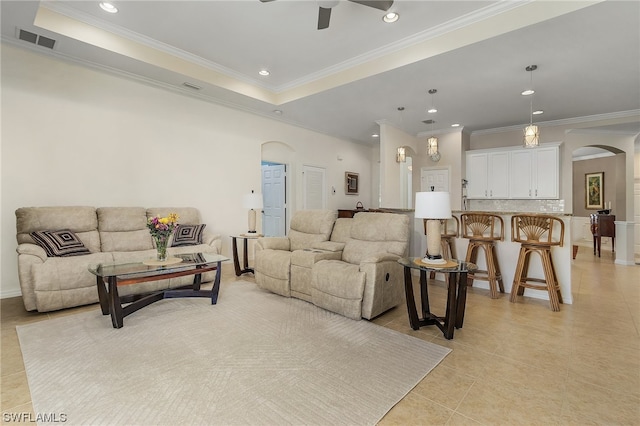 living room featuring light tile flooring, a raised ceiling, ceiling fan, and crown molding