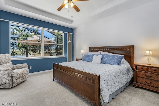 bedroom featuring light colored carpet, a raised ceiling, and ceiling fan