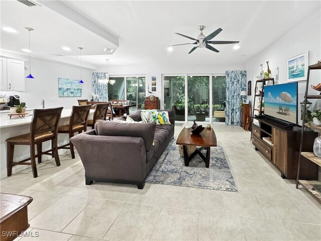 tiled living room with ceiling fan with notable chandelier