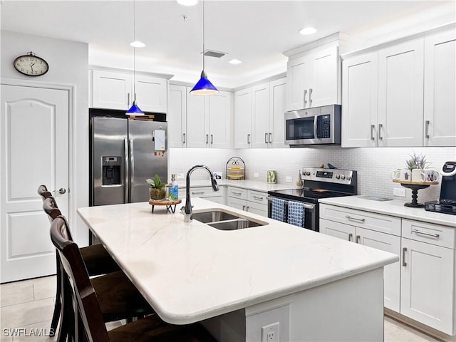 kitchen with pendant lighting, decorative backsplash, appliances with stainless steel finishes, a sink, and a kitchen bar