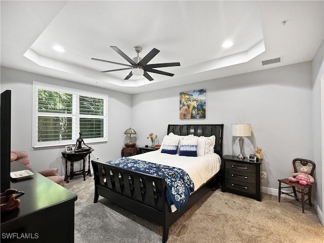 bedroom featuring light carpet, baseboards, visible vents, a raised ceiling, and a ceiling fan