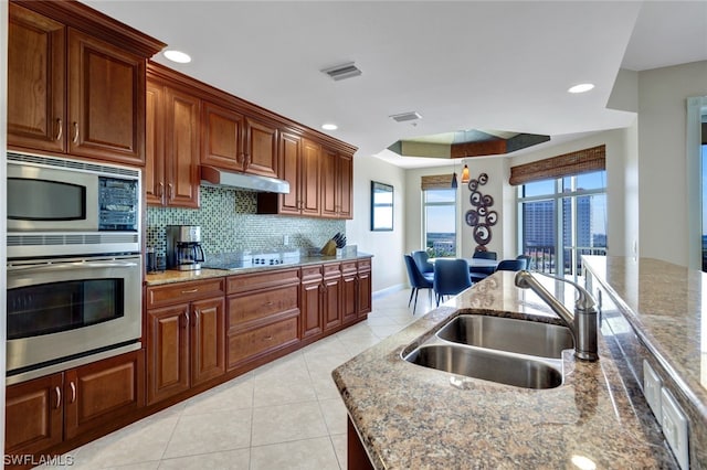 kitchen with black electric stovetop, backsplash, stainless steel oven, sink, and stone countertops