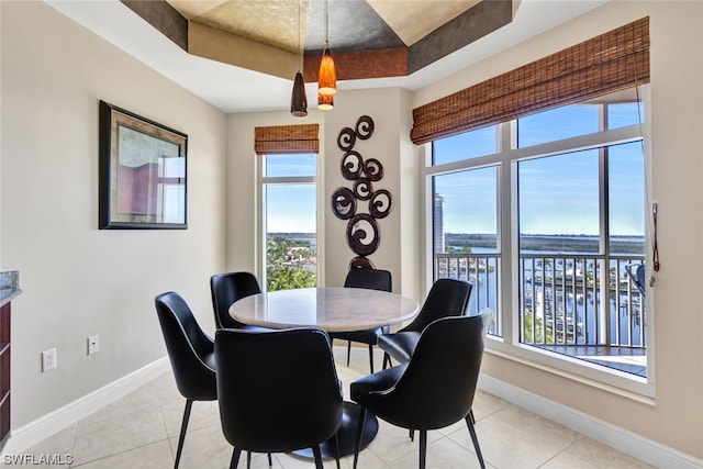 dining area with a tray ceiling, plenty of natural light, a water view, and light tile patterned flooring