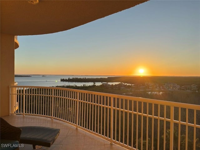 balcony at dusk featuring a water view