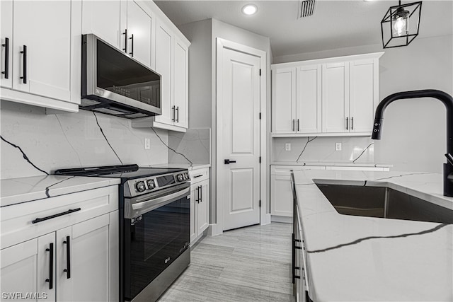 kitchen with white cabinets, appliances with stainless steel finishes, light stone countertops, and decorative light fixtures