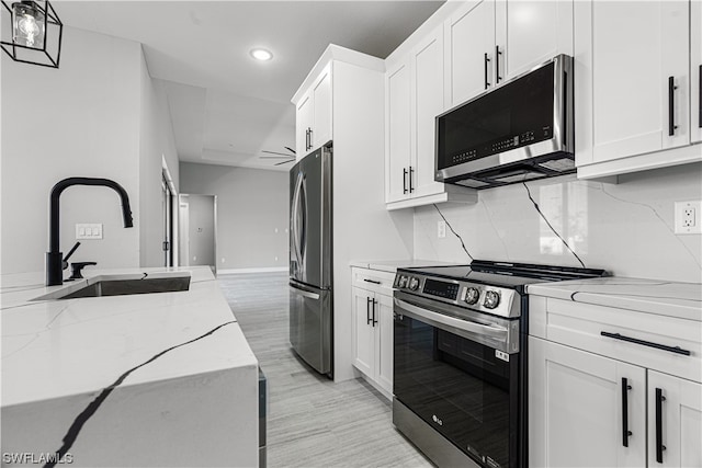 kitchen with light stone countertops, stainless steel appliances, white cabinetry, and sink