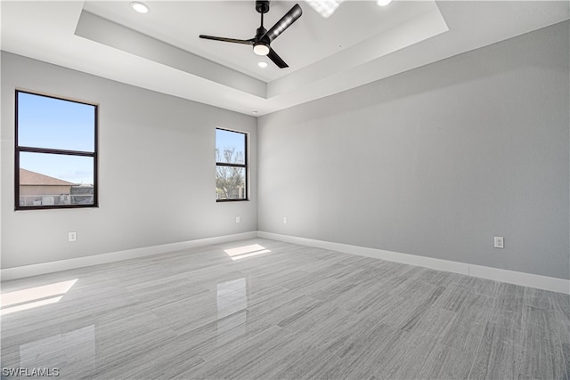 empty room featuring ceiling fan, a tray ceiling, and light wood-type flooring